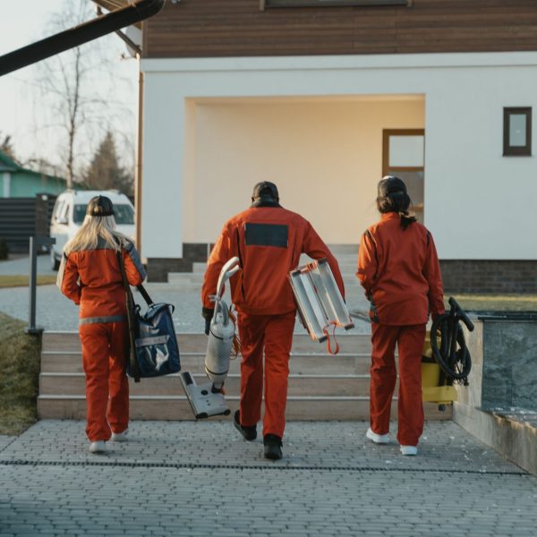 Cleaning crew in red uniforms with equipment approaching a modern house exterior.