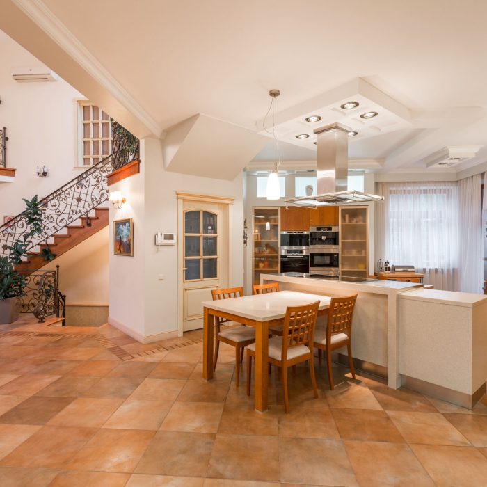 Interior of spacious apartment with open kitchen with chairs and counter near cupboards next to stairway